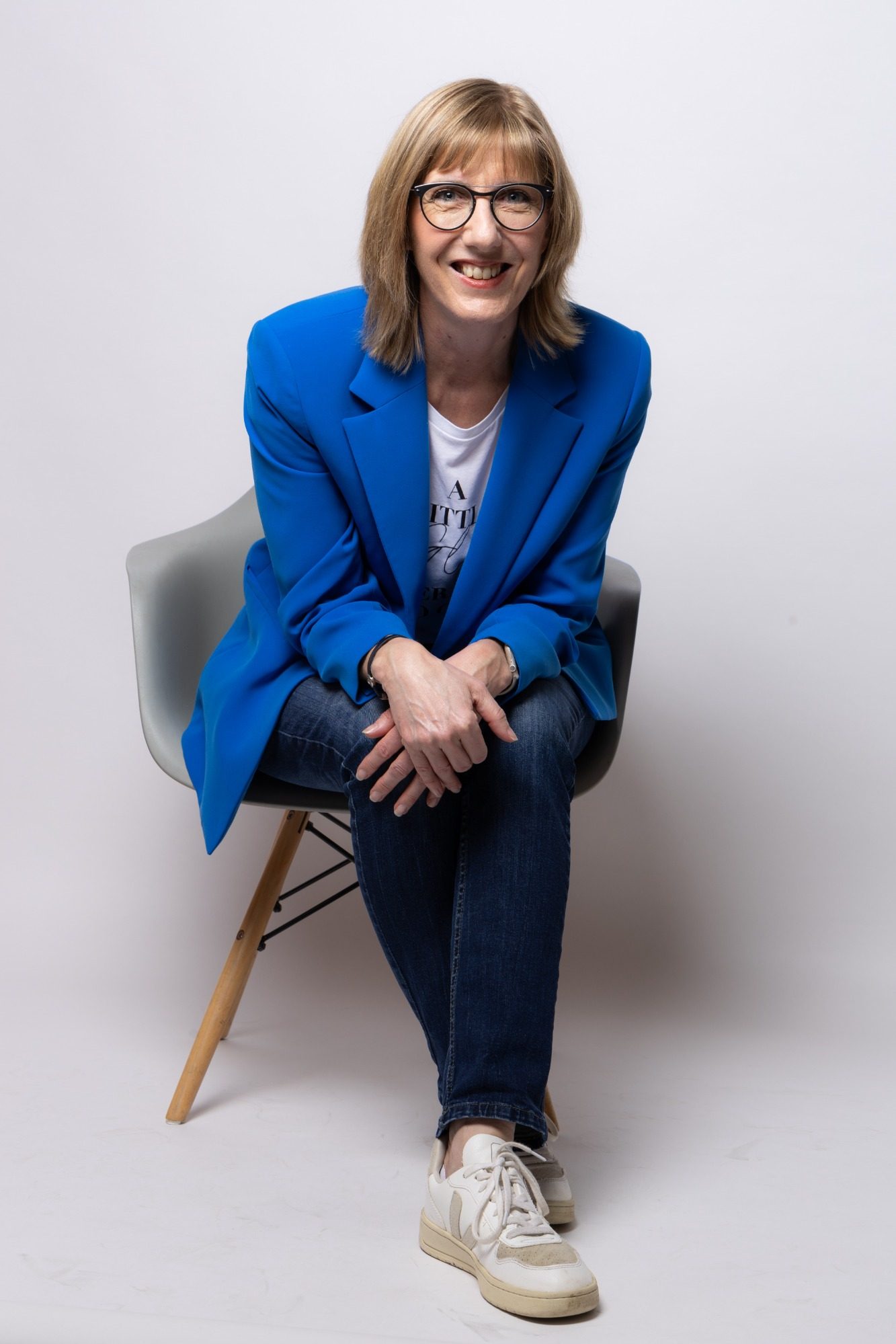 Britta Möller sitzt auf einem Stuhl und lächelt offen in die Kamra.